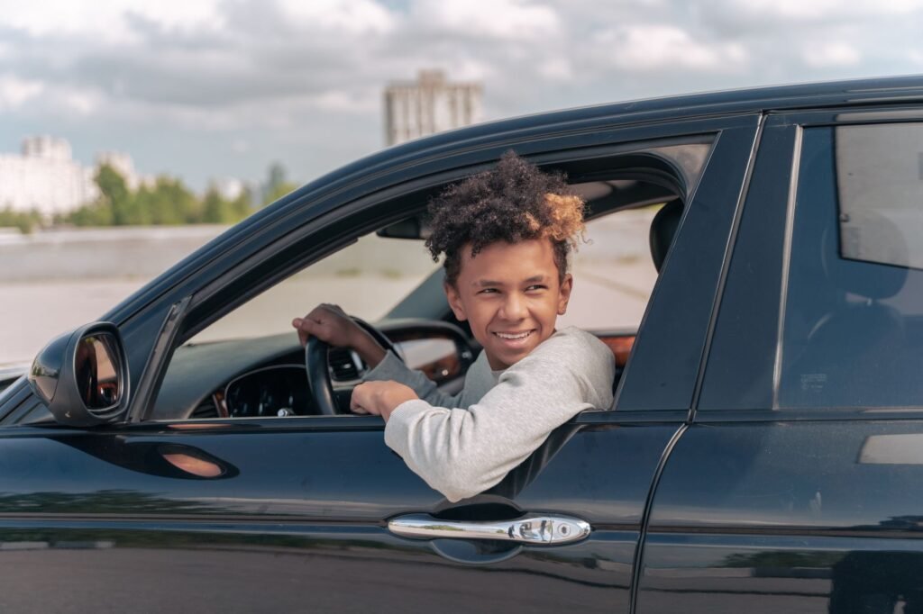 A smiling teen holding a driver's license with a car in the background. — car insurance young drivers Nevada